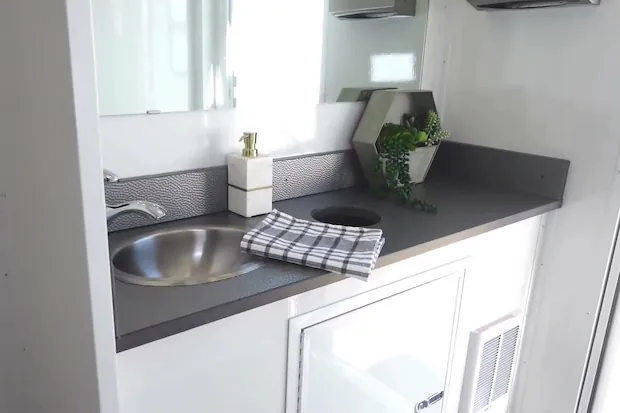 A vanity with a stainless sink on a dark counter above a white cabinet