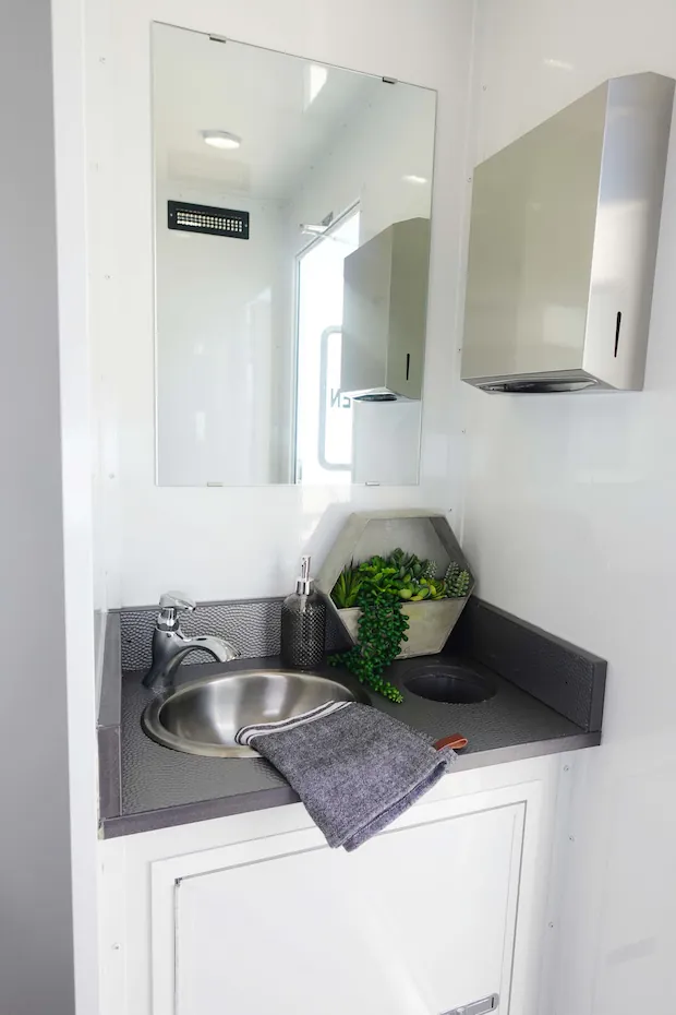 A women's restroom vanity with a stainless sink, an oversized mirror and a paper towel dispenser